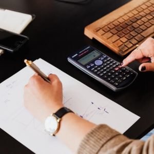crop woman using calculator and taking notes on paper